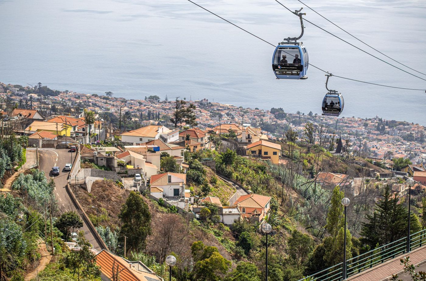A red cable car carriage moving up a steep hillside towards the village of Monte overlooking Funchal.