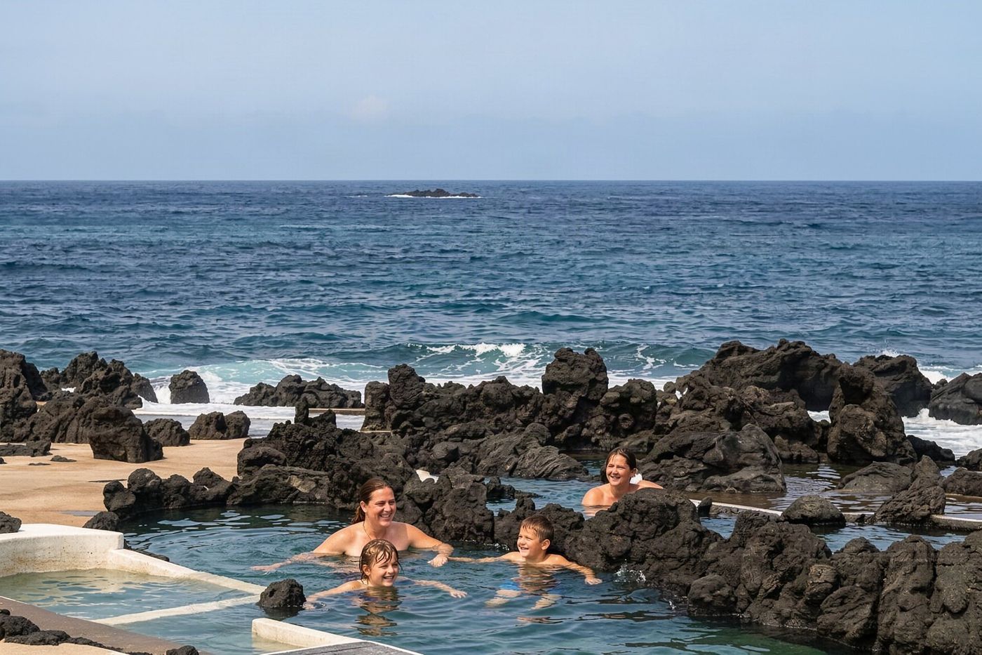 People swimming in clear water surrounded by dark volcanic rock formations.