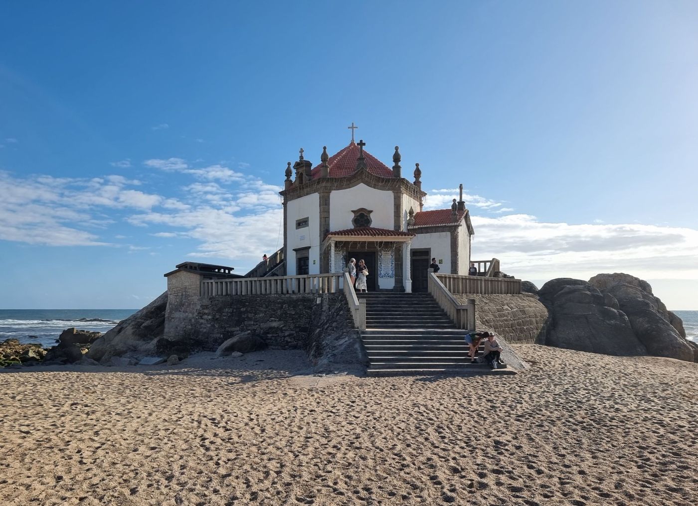 The white-walled Capela de Nossa Senhora da Conceição stands near the busy harbour in Câmara de Lobos with fishing boats visible in the water.