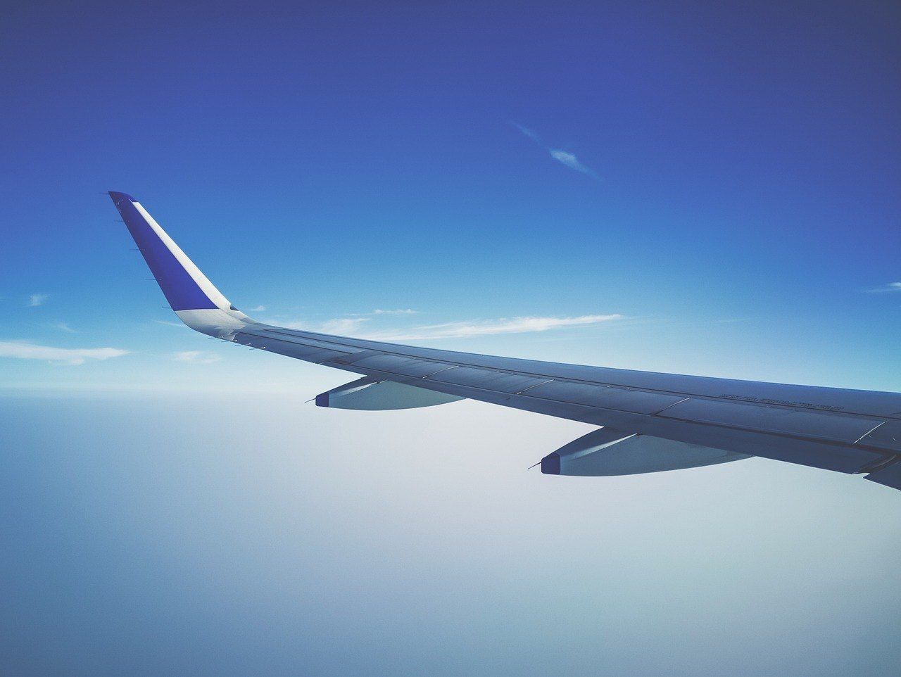 View from an aeroplane window showing white clouds below and the wing against a blue sky.