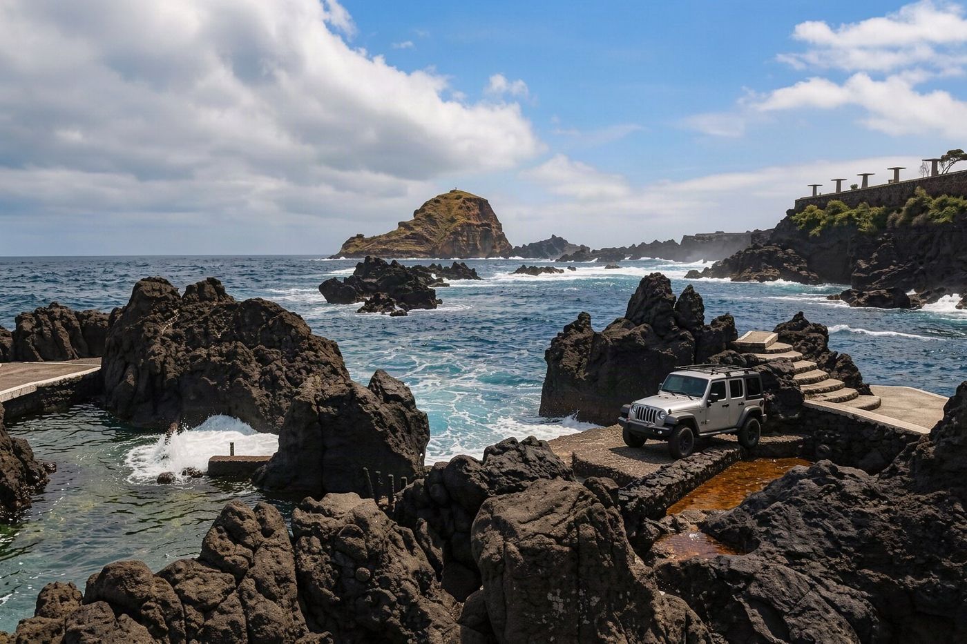 A jeep tour vehicle is parked near the natural volcanic swimming pools at Porto Moniz.