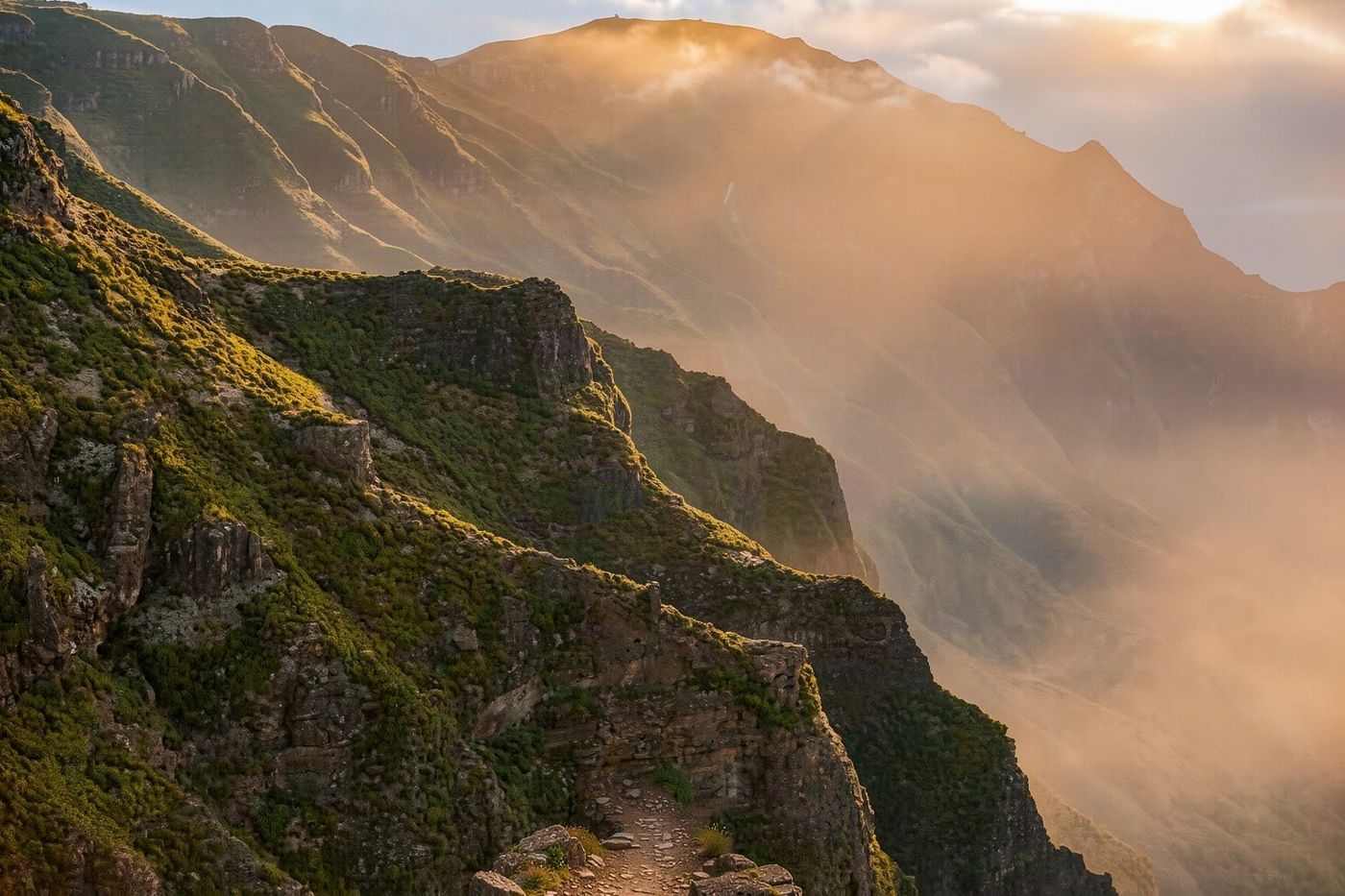 Hikers walking along a narrow stone ridge path with steep drops on either side in the central mountains.