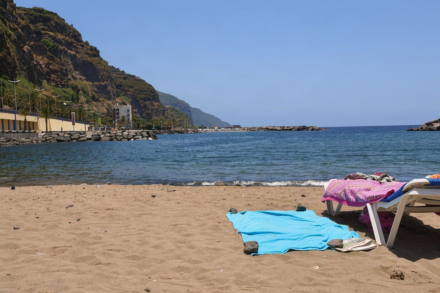 A curved sandy beach backed by cliffs and buildings in the town of Machico on the east coast of Madeira.