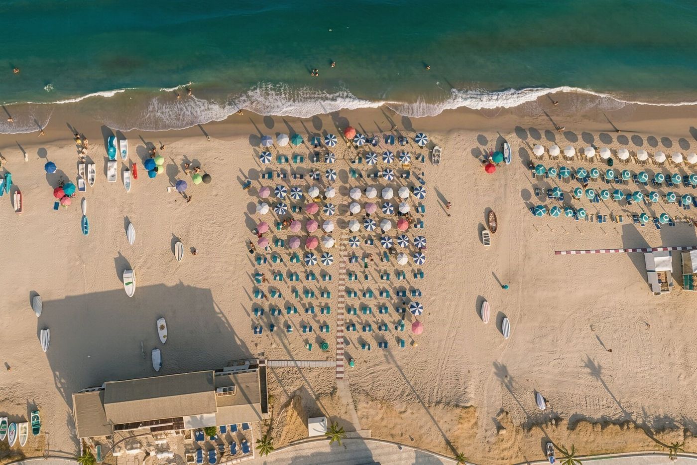 Rows of empty sunbeds and umbrellas waiting for visitors on a sandy beach.