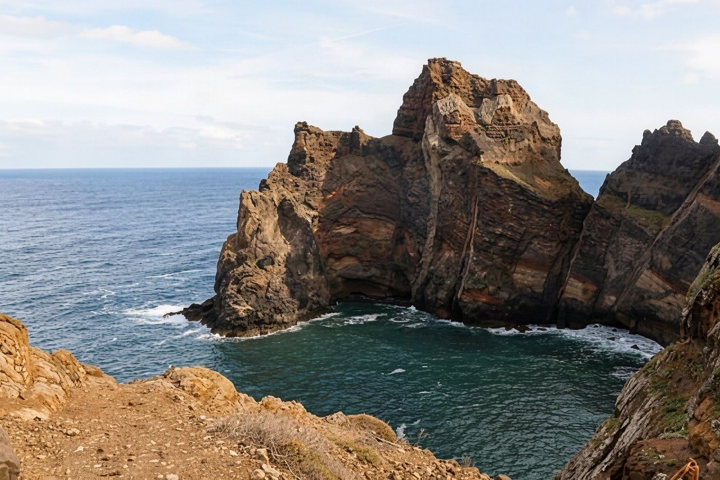 A pebble beach nestled at the foot of a cliff with clear turquoise water.