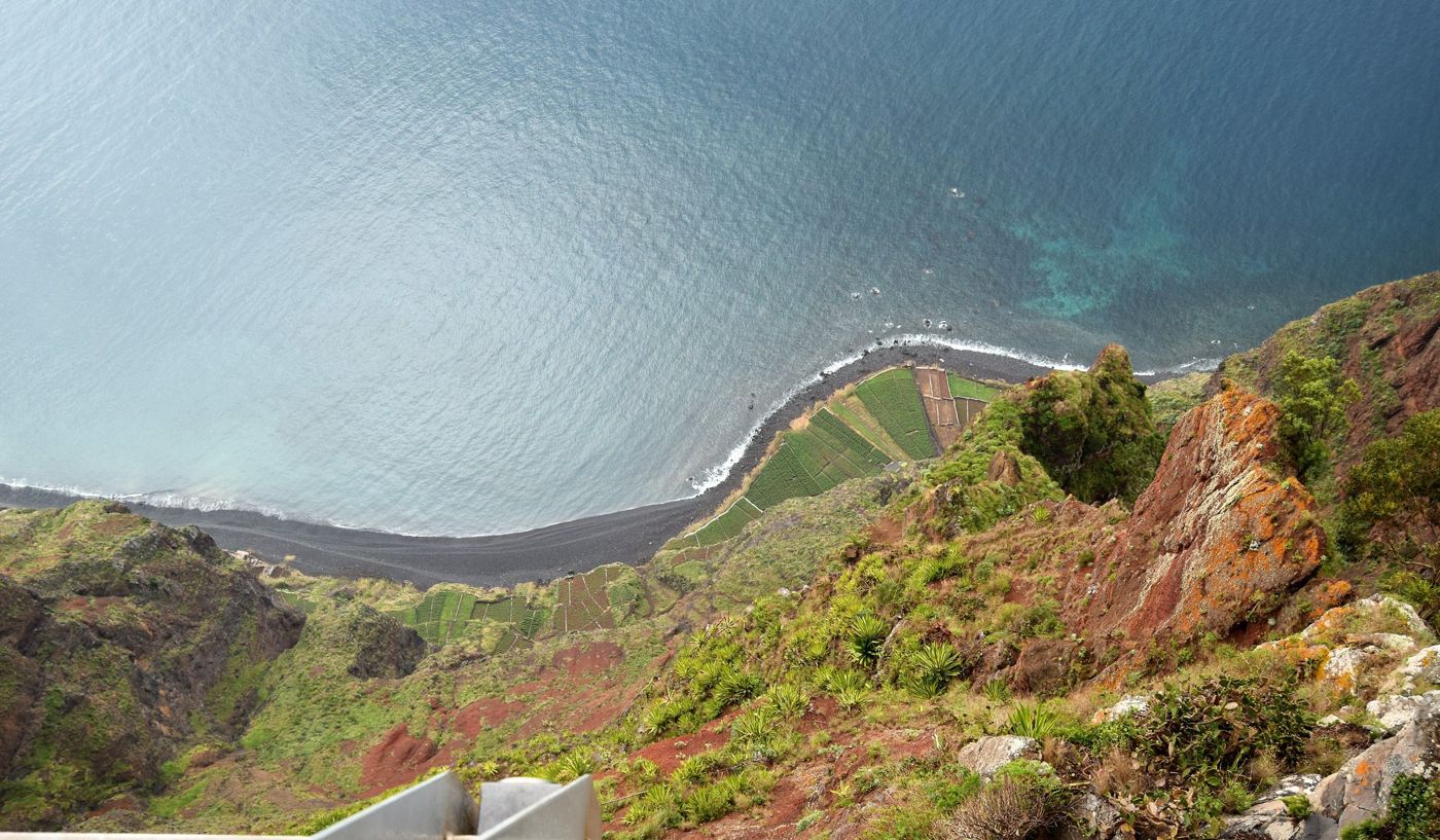Visitors standing on the suspended glass floor looking down the steep cliff face at Cabo Girão.