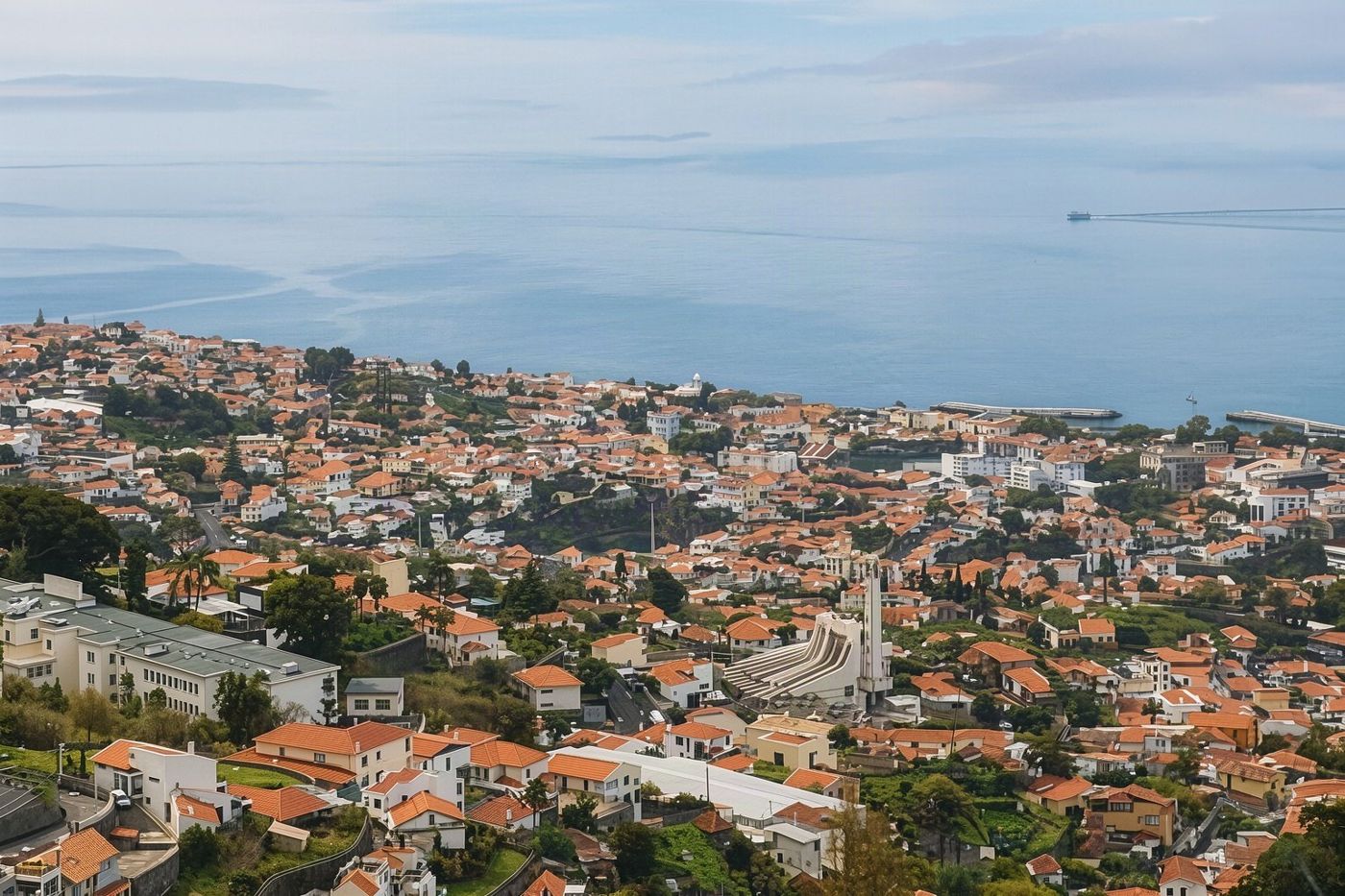 An aerial perspective of the historic red-tiled roofs of Funchal's old town and the blue sea.